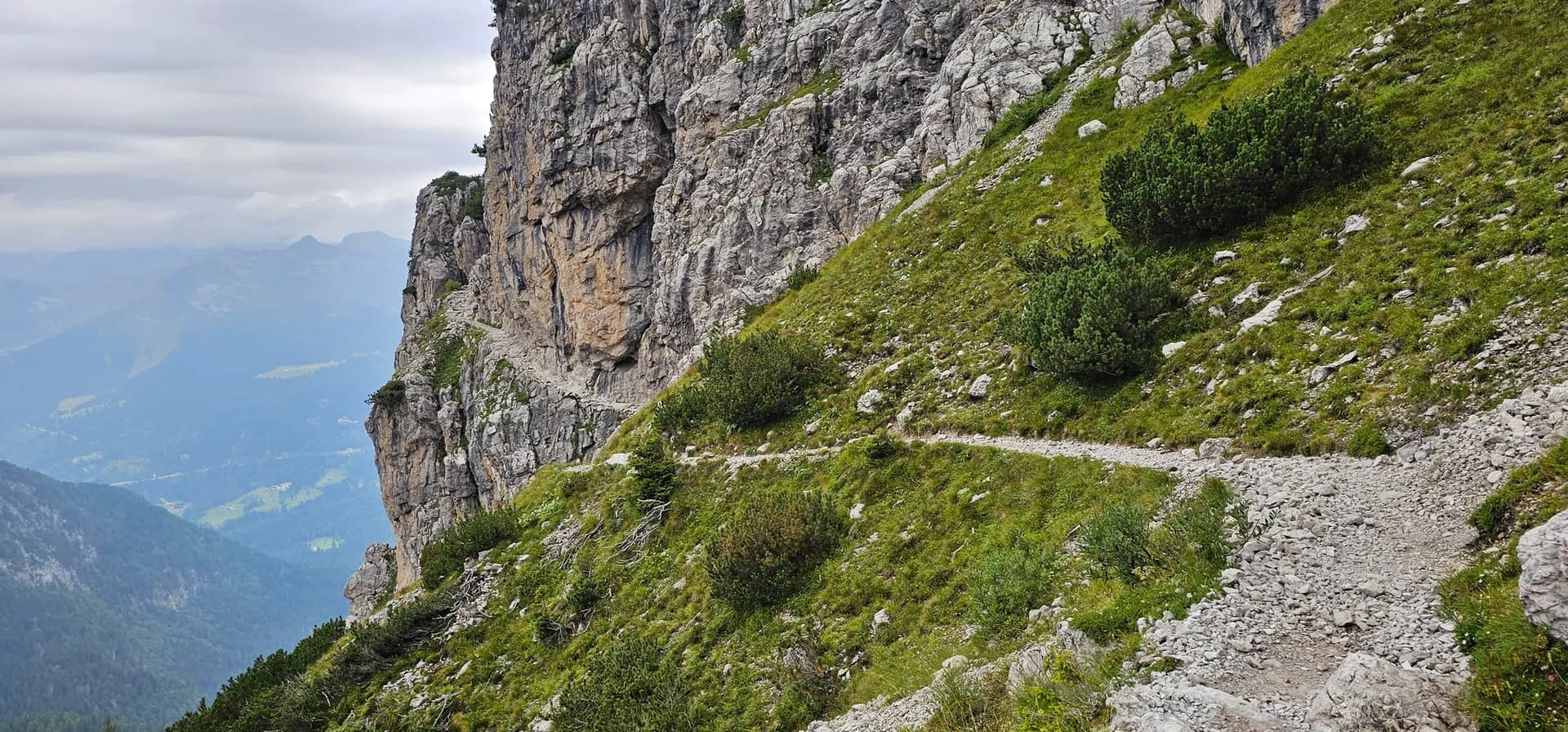 Hiking trail along a steep rocky cliff in Adamello-Brenta Nature Park with mountain valley views.