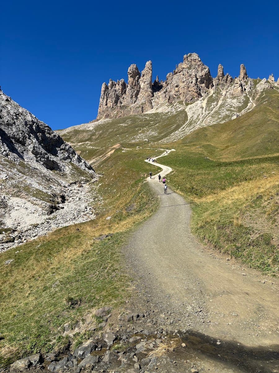 Hikers walking on winding dirt path through alpine mountain landscape under clear blue sky