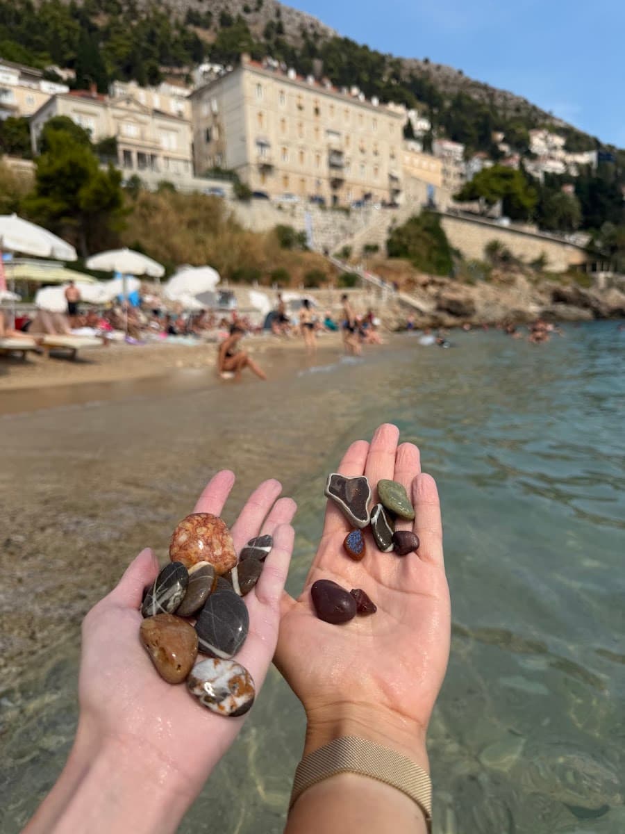 Hands holding colorful beach stones with coastal town and beach in the background
