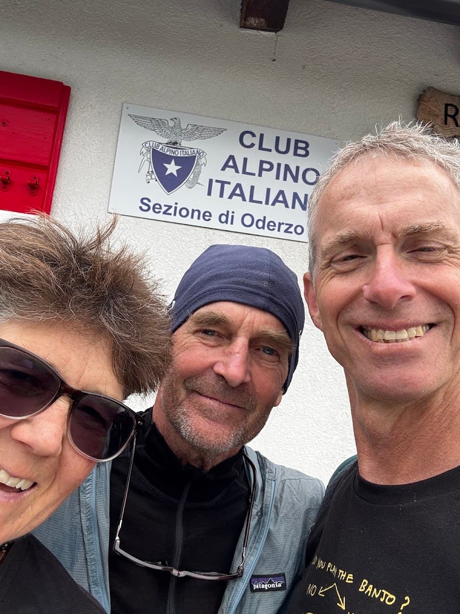 Three smiling people taking a selfie in front of a Club Alpino Italiano sign in Oderzo