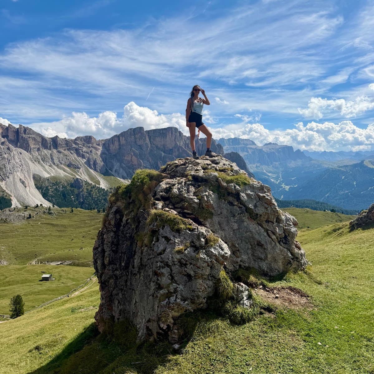 Hiker standing on a large rock in alpine mountain landscape with green valley and blue sky