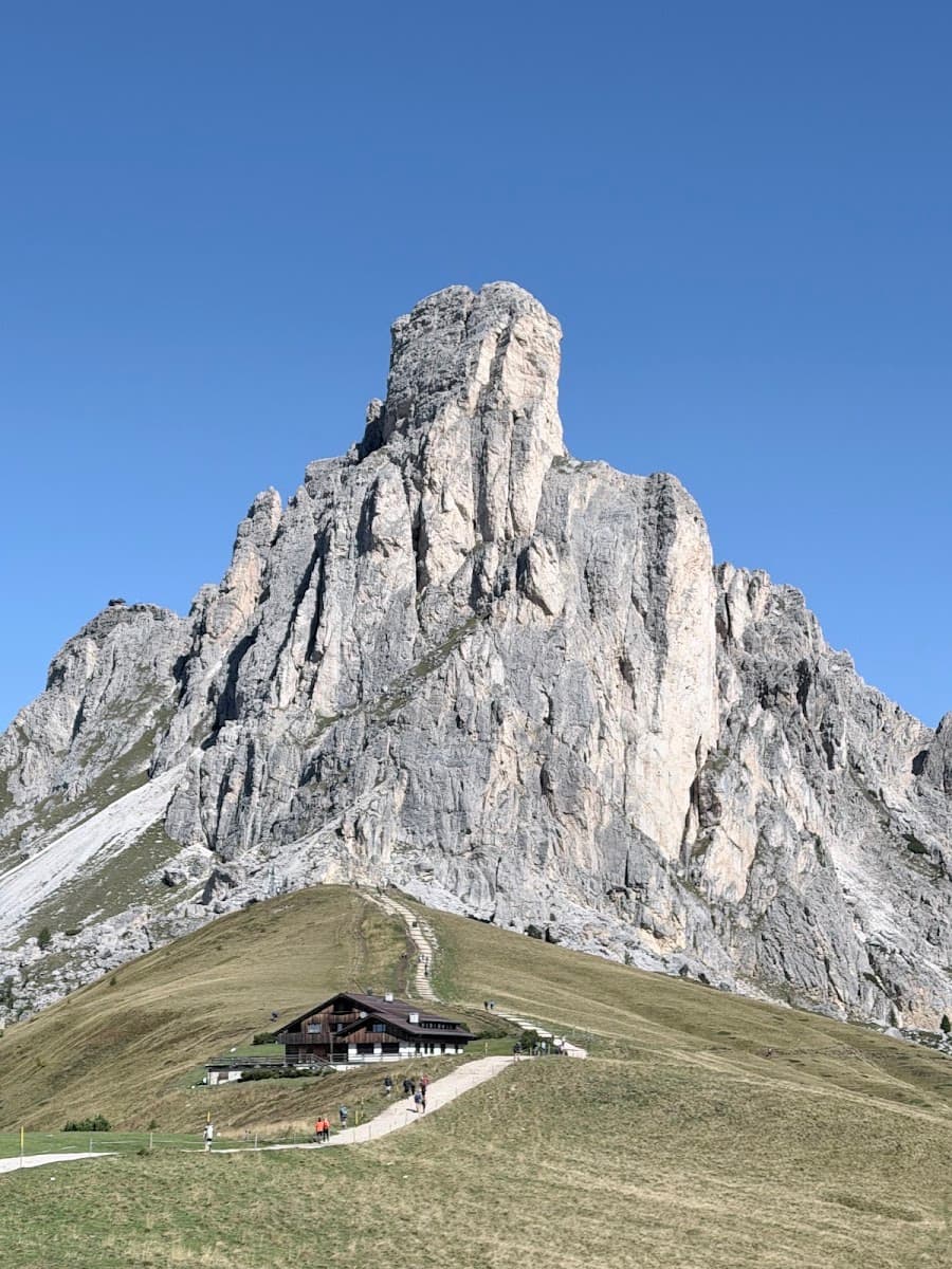Mountain peak with rocky cliffs and a building on grassy hillside below