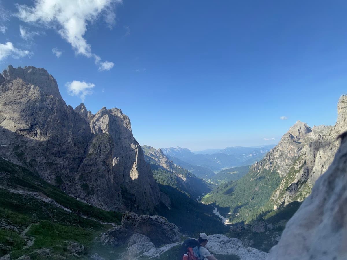 Hiker with backpack overlooking mountain valley and rocky peaks under blue sky