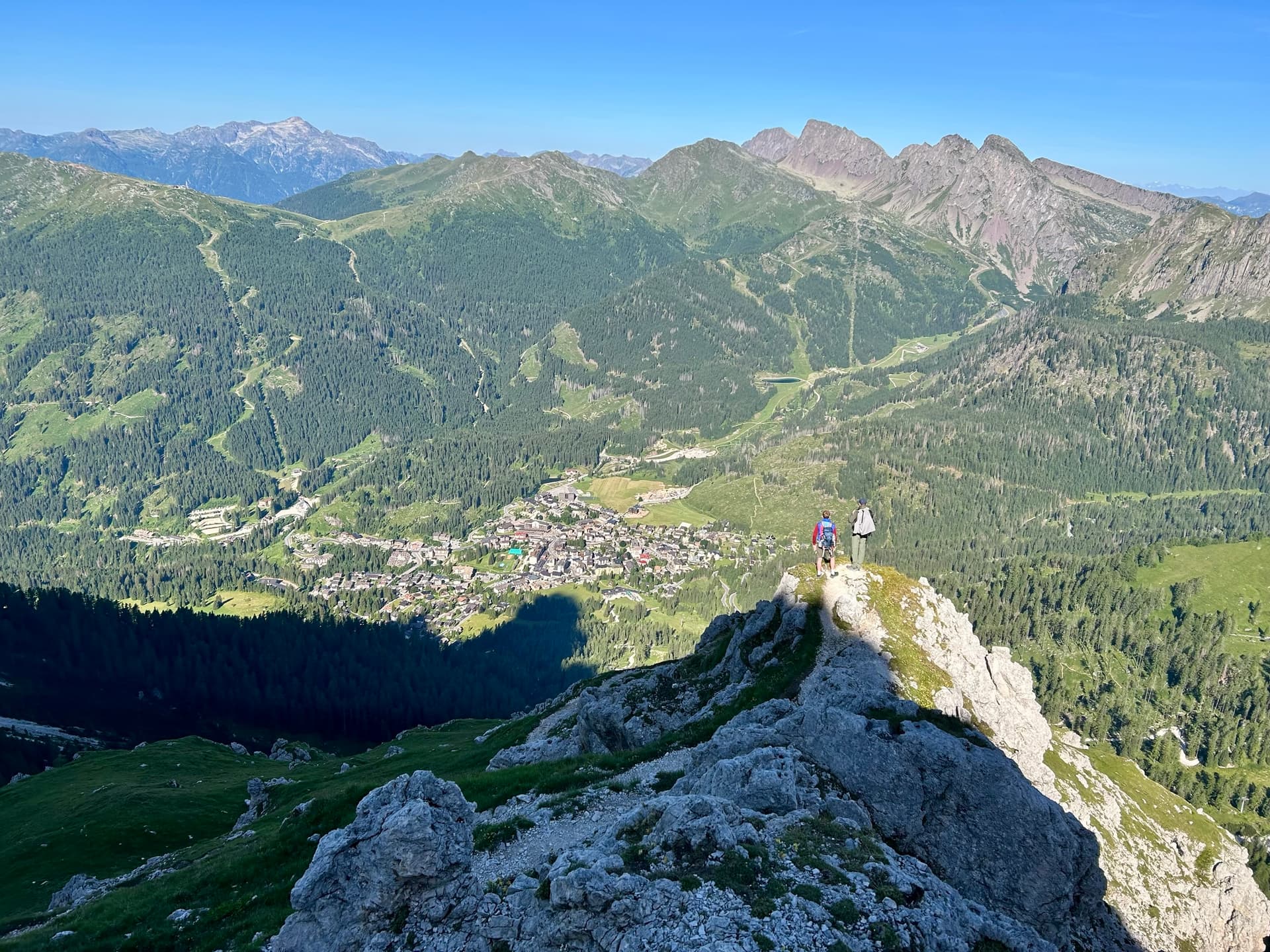 Hikers on a rocky mountain ridge overlooking a valley village and alpine peaks