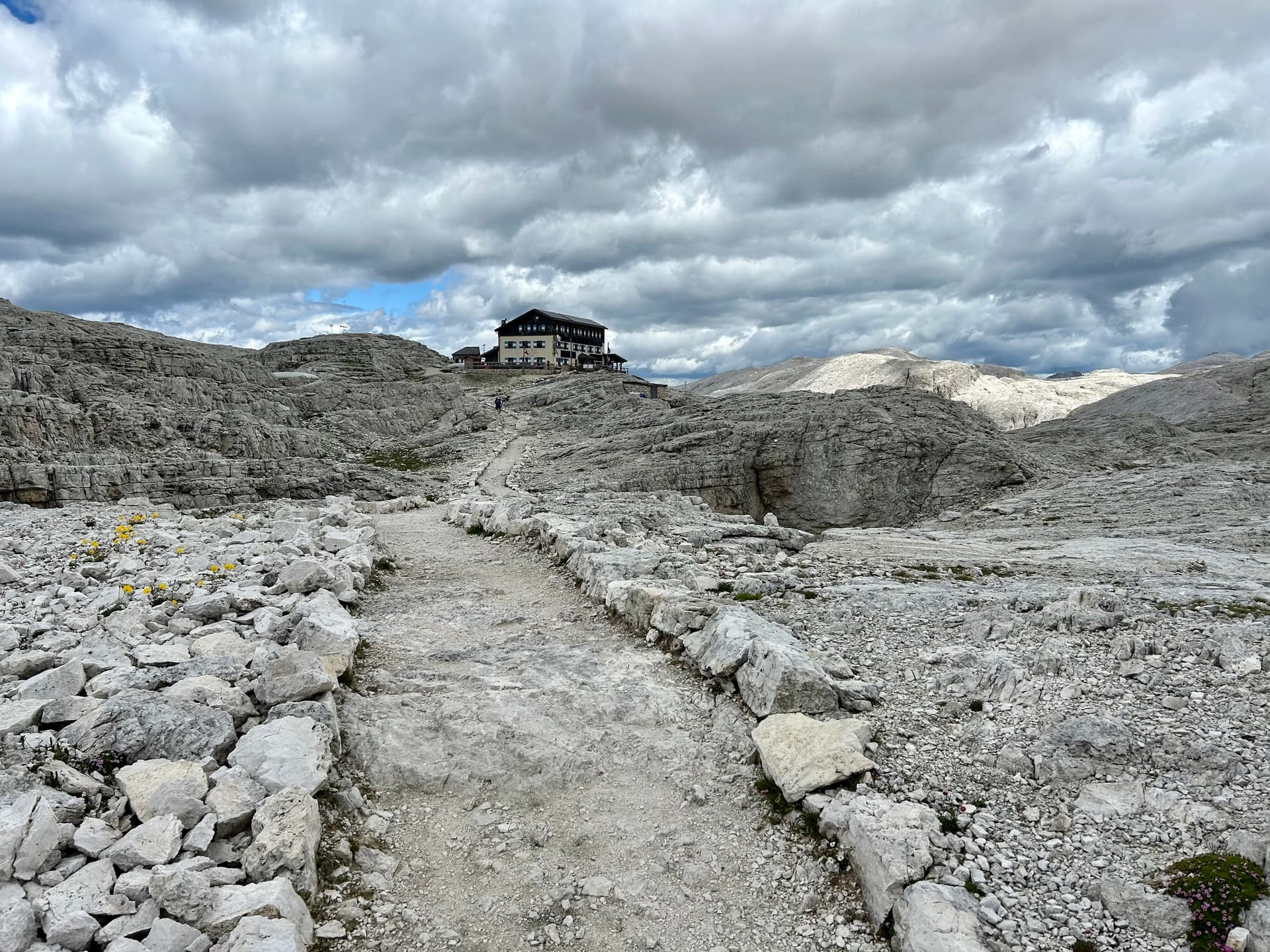 Mountain hut on rocky plateau with stone path under cloudy sky