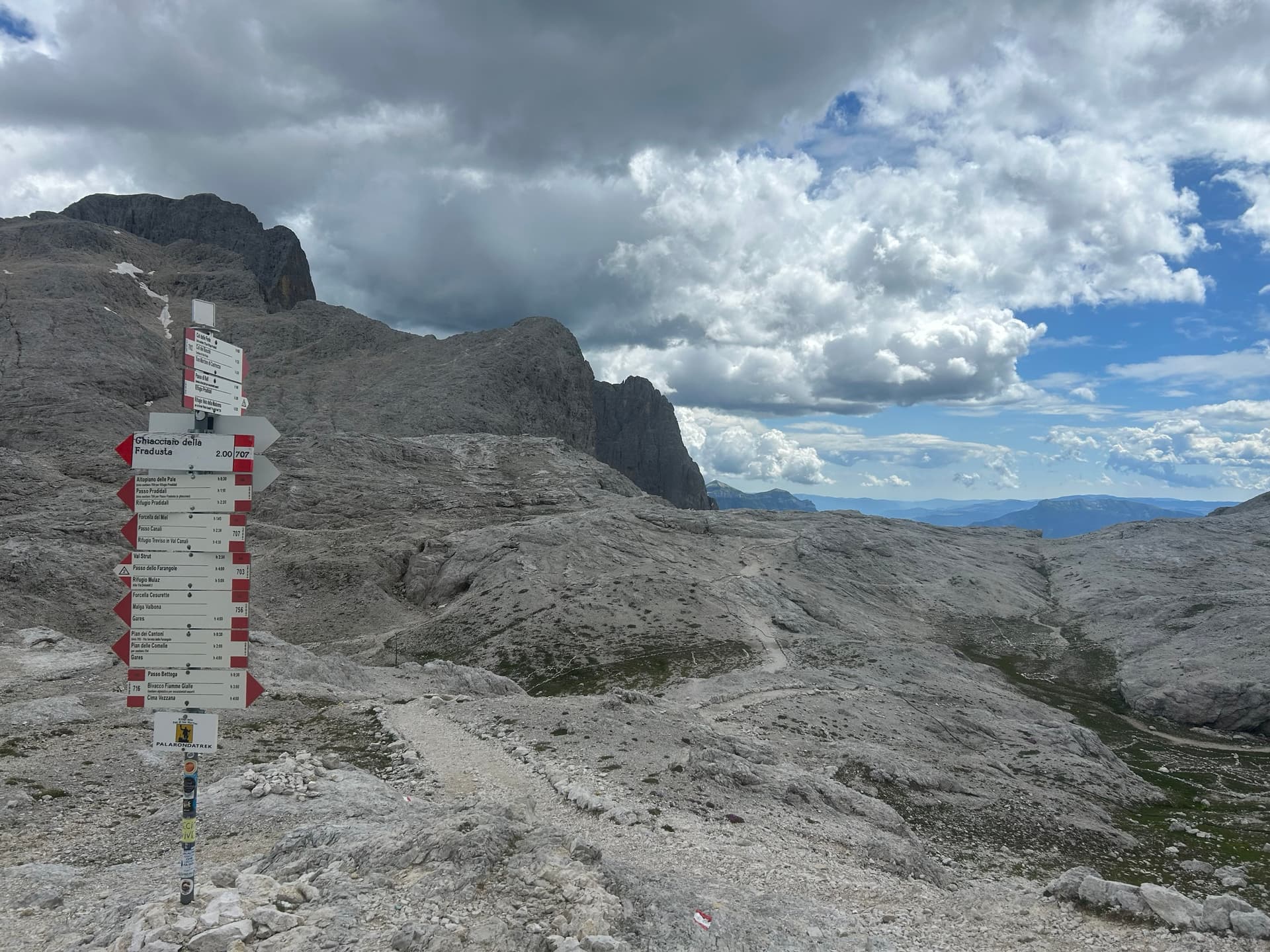 Trail signpost on rocky alpine plateau with hiking paths and mountains under cloudy sky