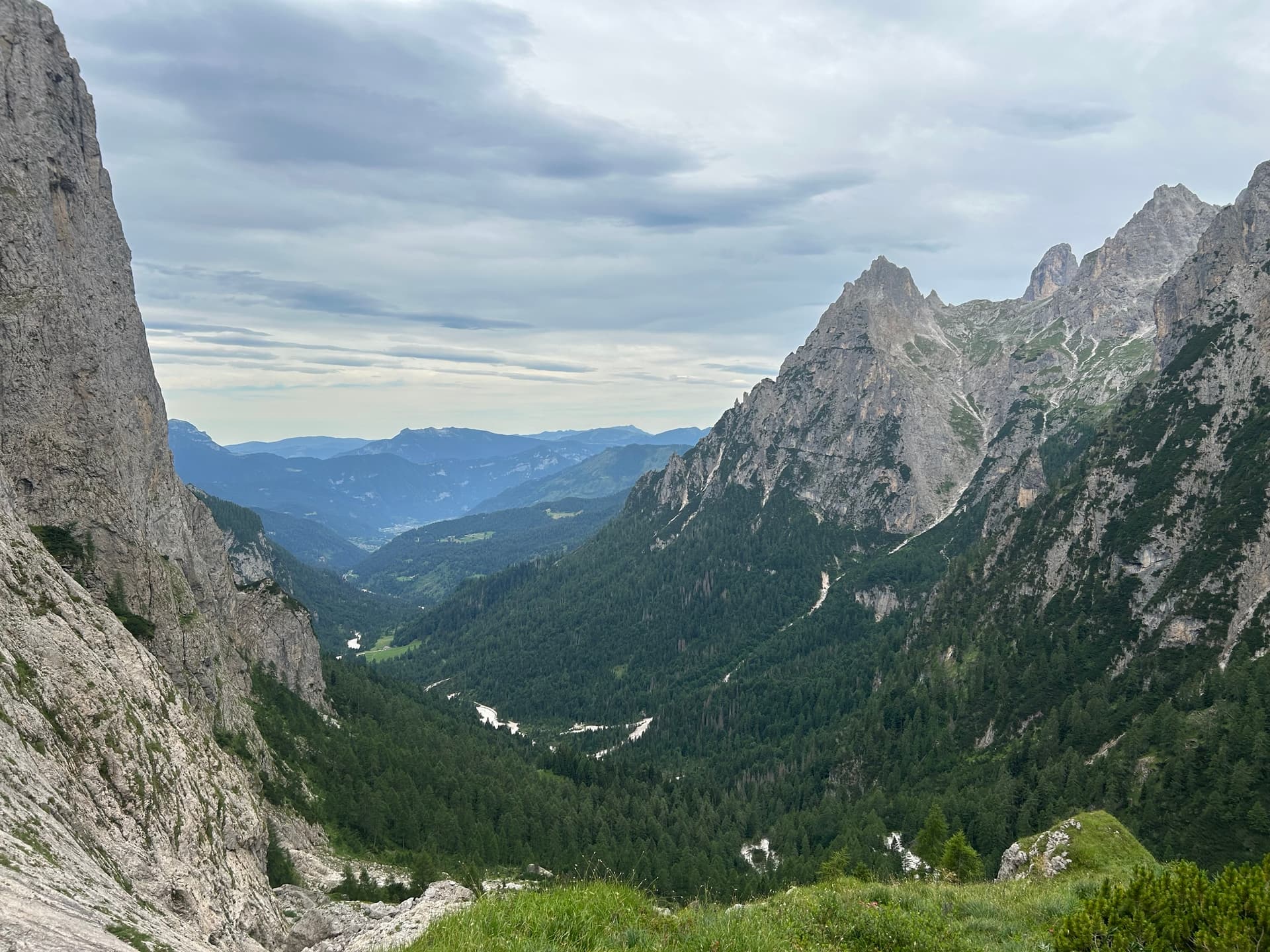 Deep valley with green pine forest below steep mountain cliffs under an overcast sky