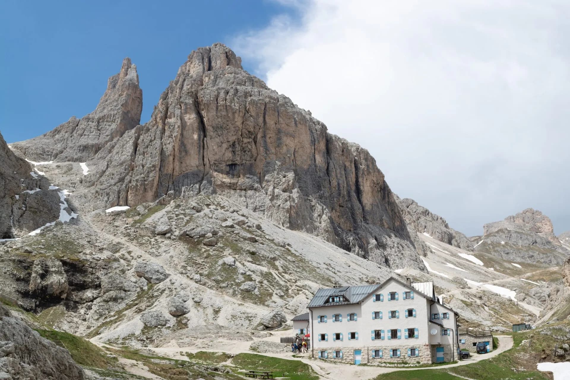 Mountain hut at the base of massive rocky peaks in the Dolomites with patches of snow.