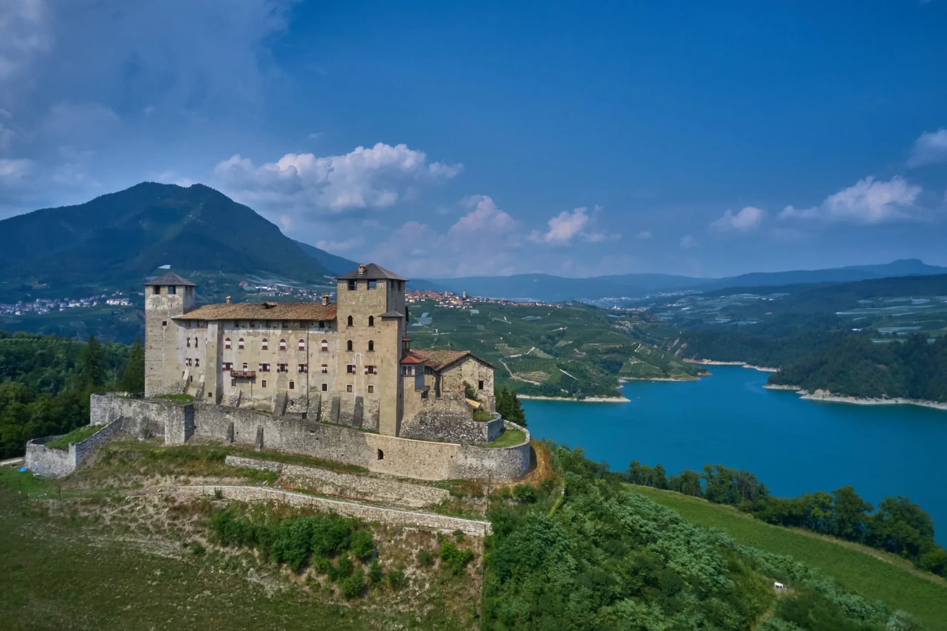 Castel Cles overlooking Lake Santa Giustina with mountains and terraced hillsides.