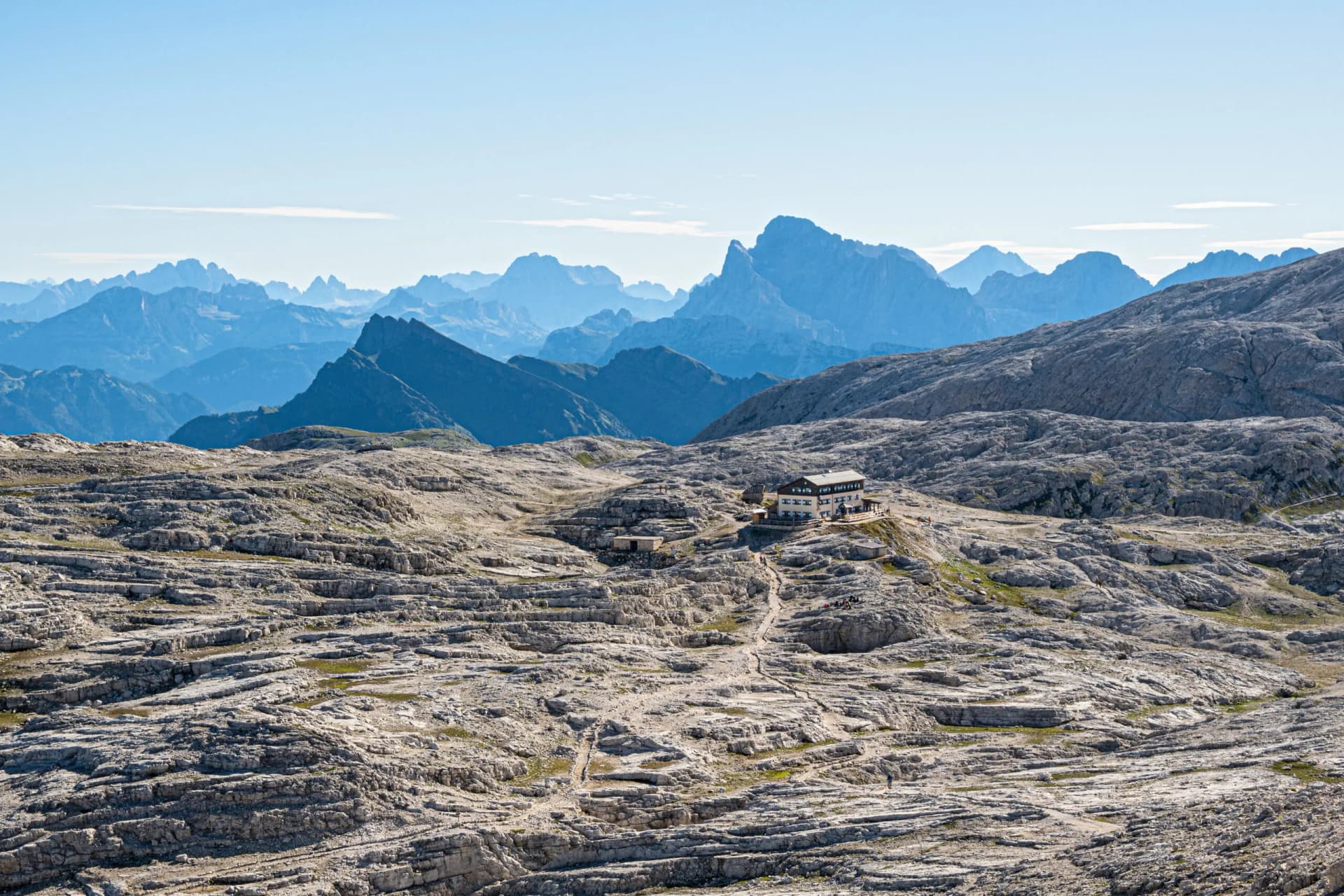 Mountain refuge Rifugio Rosetta on rocky terrain with layered limestone and blue mountain ranges.