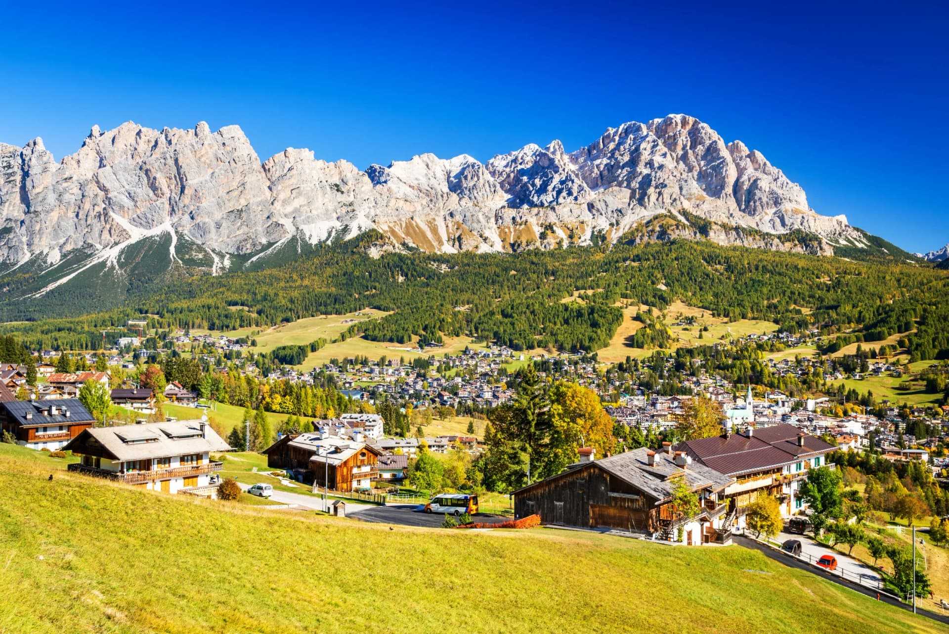 Alpine village nestled below rugged, rocky mountains under a clear blue sky in Cortina d'Ampezzo.