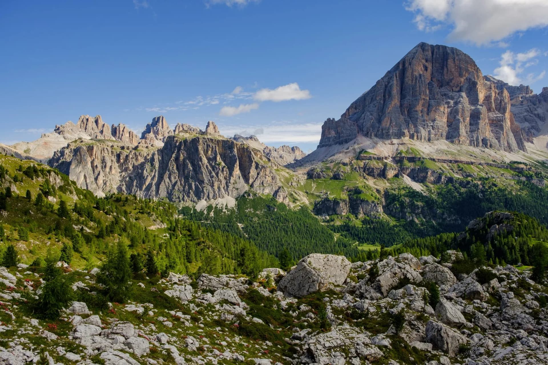 View of Tofana di Rozes mountain with rocky foreground and green slopes under blue sky.