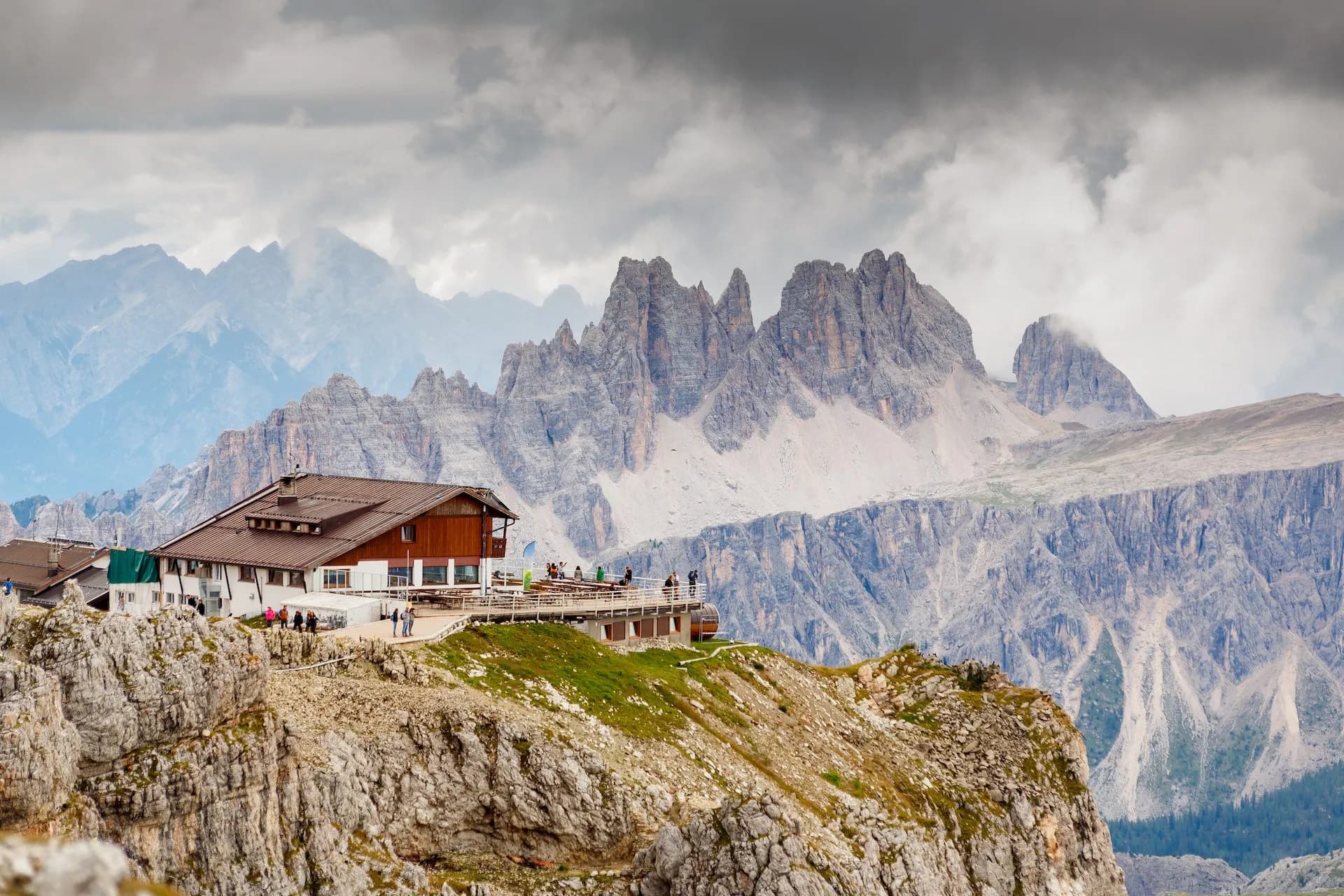 Rifugio Lagazuoi mountain hut on rocky ridge with jagged Dolomite peaks under cloudy sky.