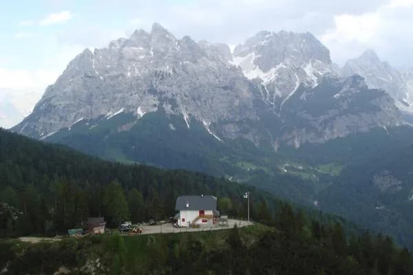 Rifugio Carestiato hut nestled on a hillside below rugged, snow-dusted alpine mountains.