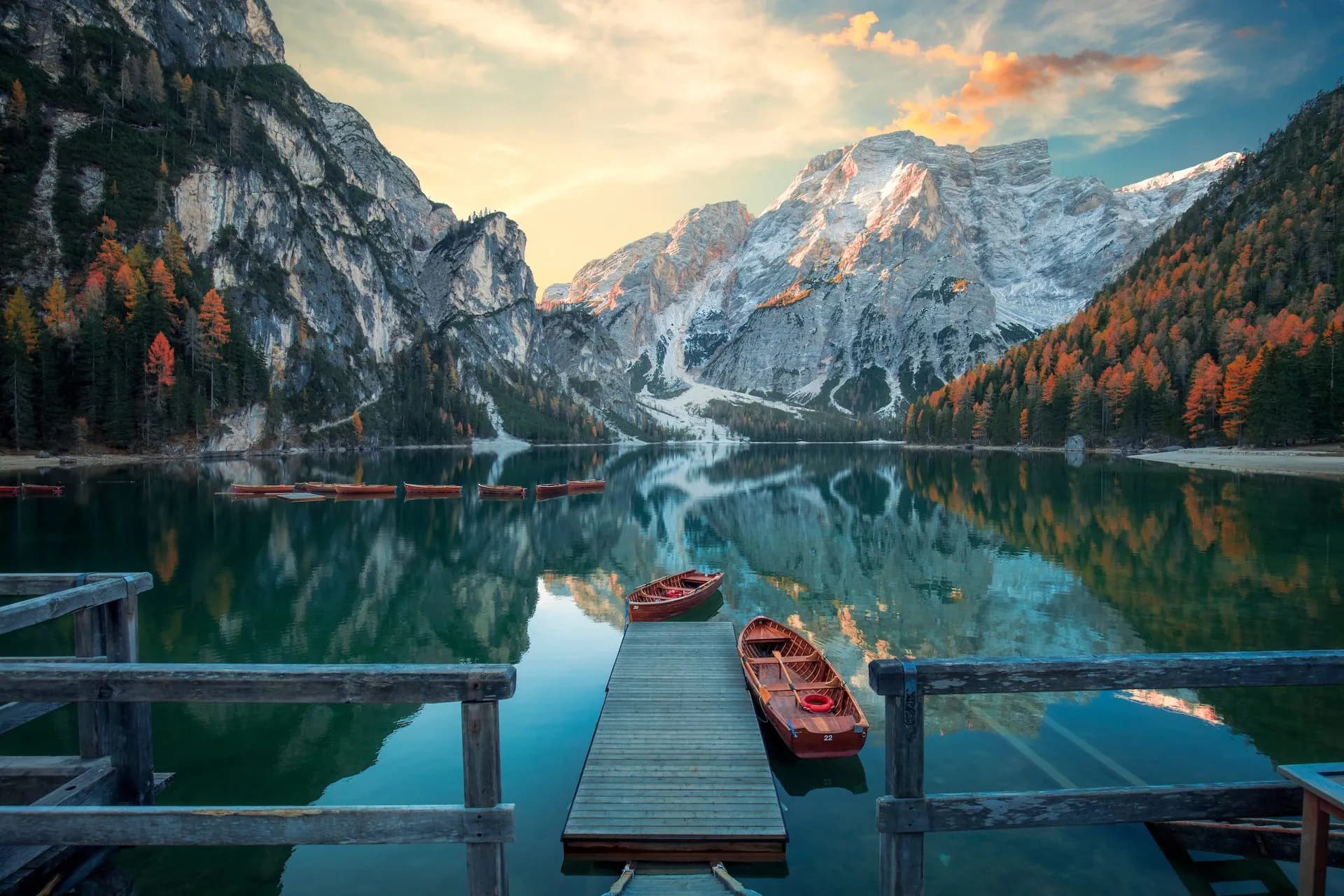 Wooden rowboats docked at pier on Lago di Braies with mountains and autumn trees reflected.