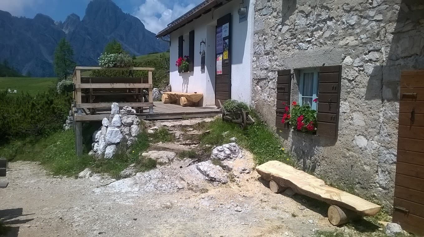 Stone mountain hut Rifugio Sommariva al Pramperet with wooden benches and alpine peaks.