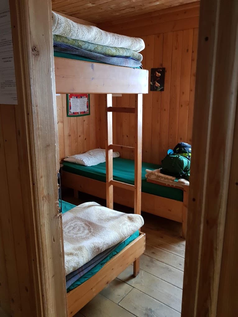Wooden bunk beds and single beds inside a rustic mountain refuge room with pine paneling.