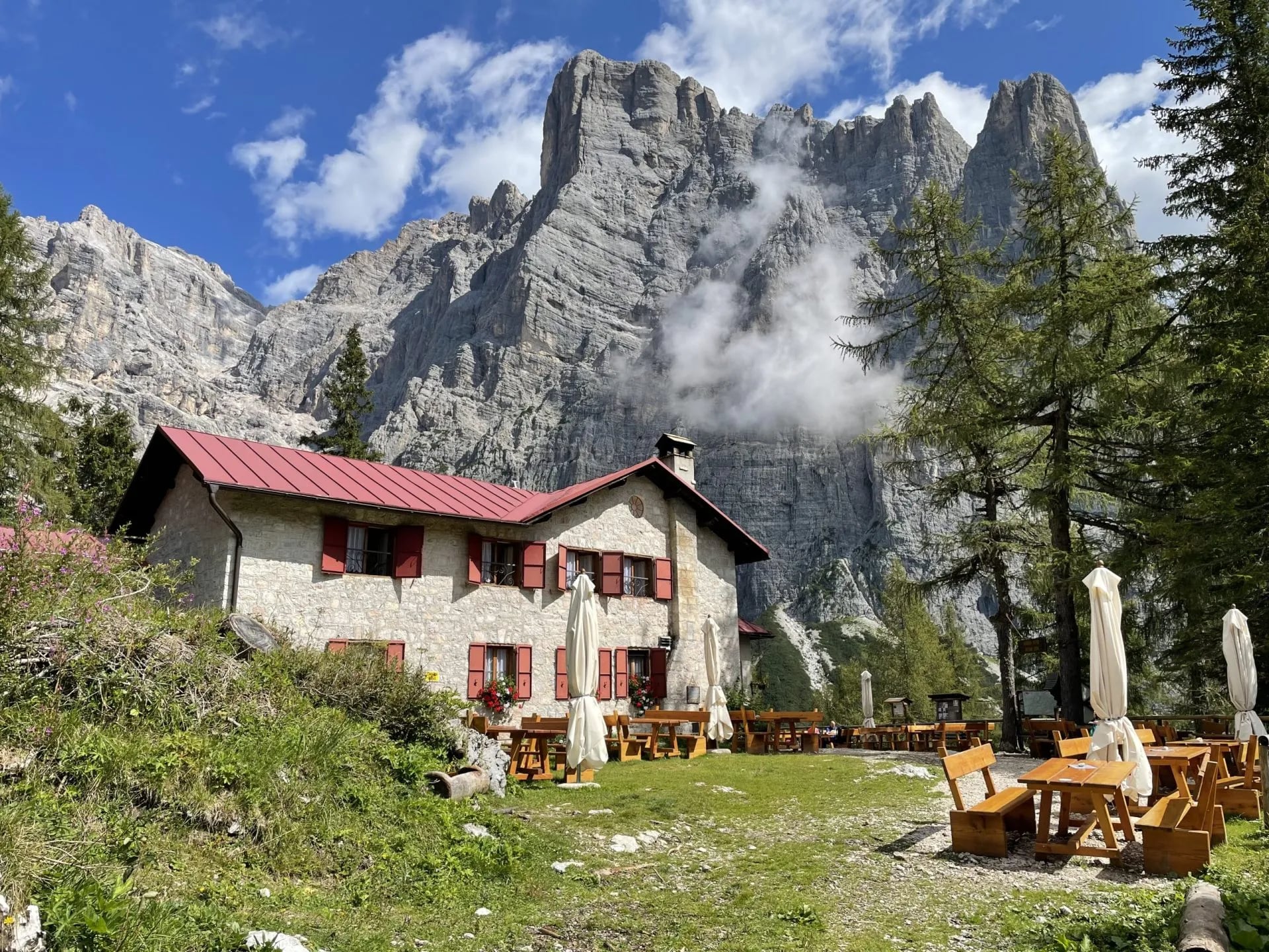 Rifugio Vazzoler stone hut with red roof below dramatic rocky mountains and clouds