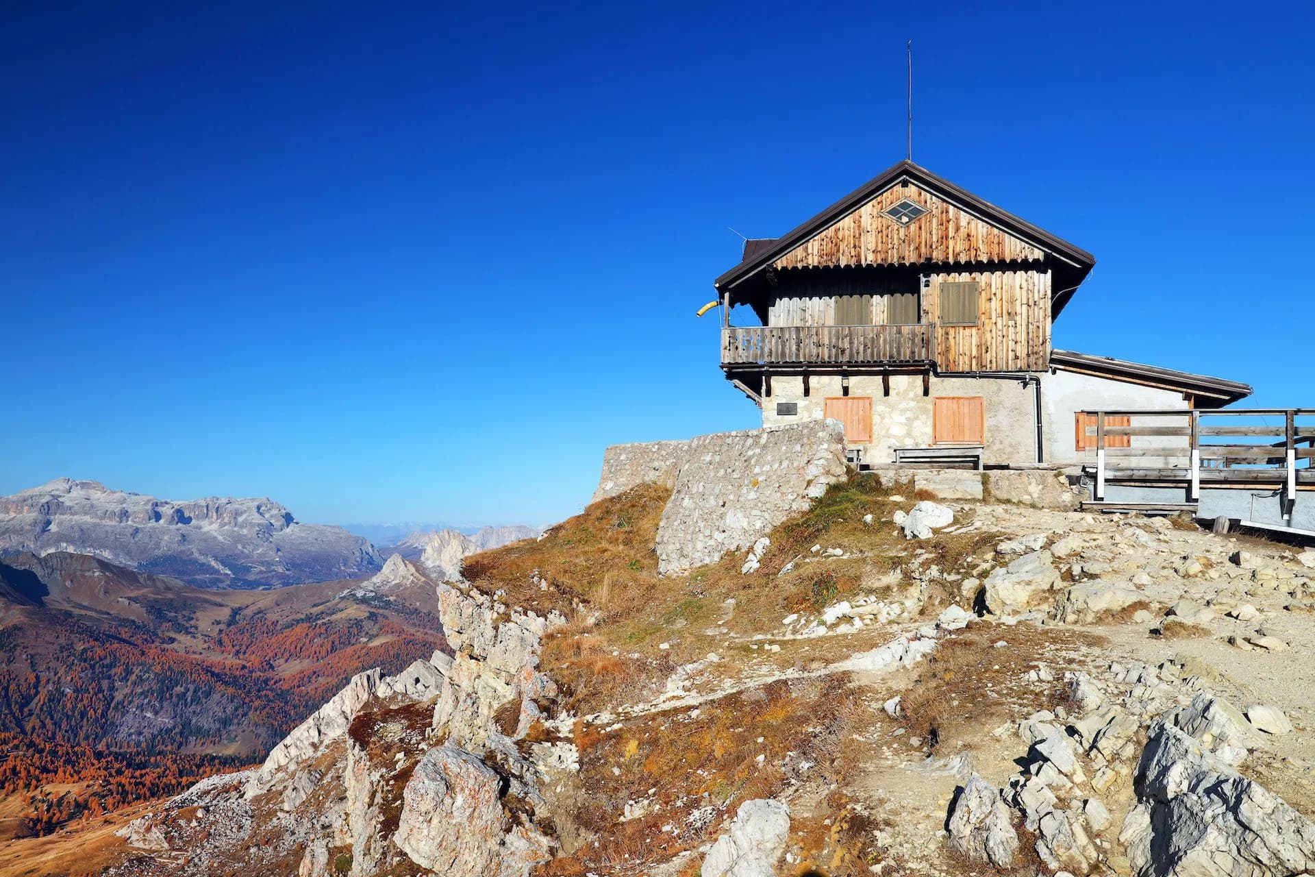 Rustic Rifugio Nuvolau mountain hut perched on rocky terrain overlooking autumn alpine valleys.