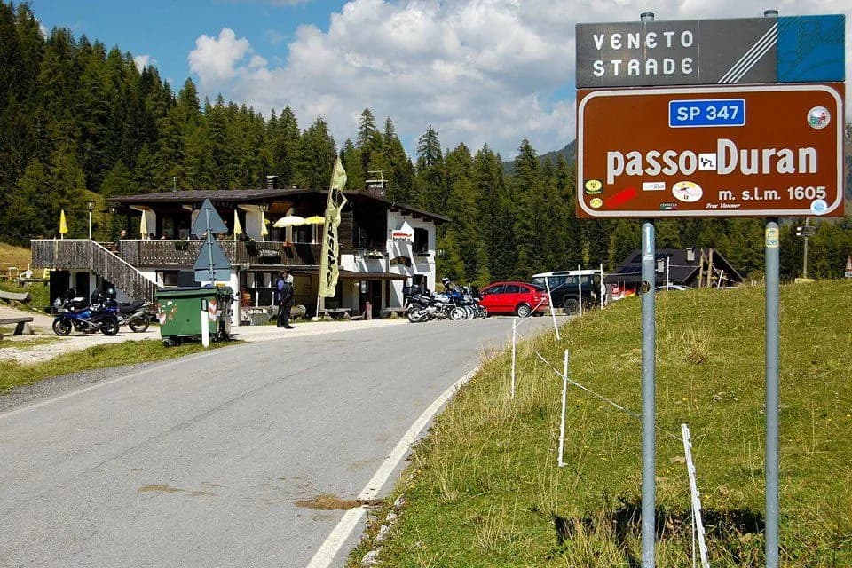 Passo Duran sign near mountain refuge with motorcycles parked by the road.