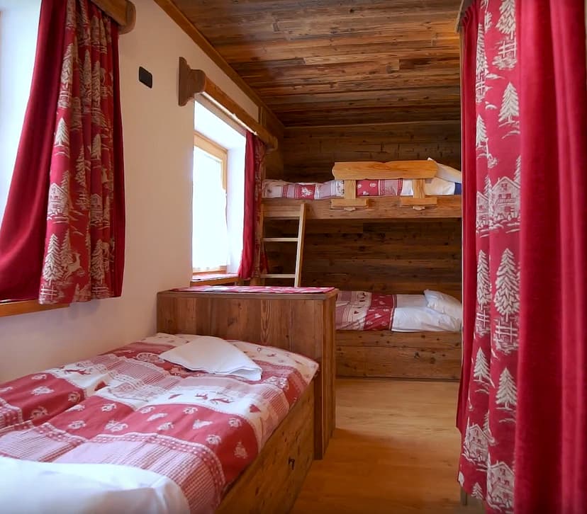 Rustic wooden mountain cabin bedroom with bunk beds and red patterned bedding at Rifugio Col Gallina.