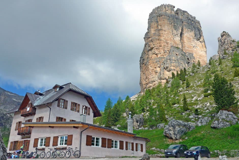 Rifugio 5 Torri mountain hut with bicycles parked outside beneath a massive rock spire.