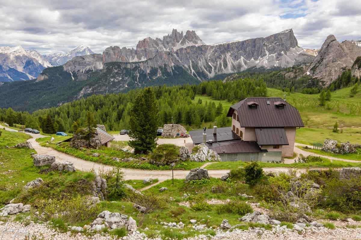 Rifugio Cinque Torri mountain hut with rocky peaks and green forest under cloudy sky.
