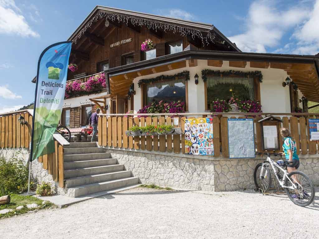Rifugio Fedare mountain hut with flowers, steps, and a mountain biker with a bicycle.