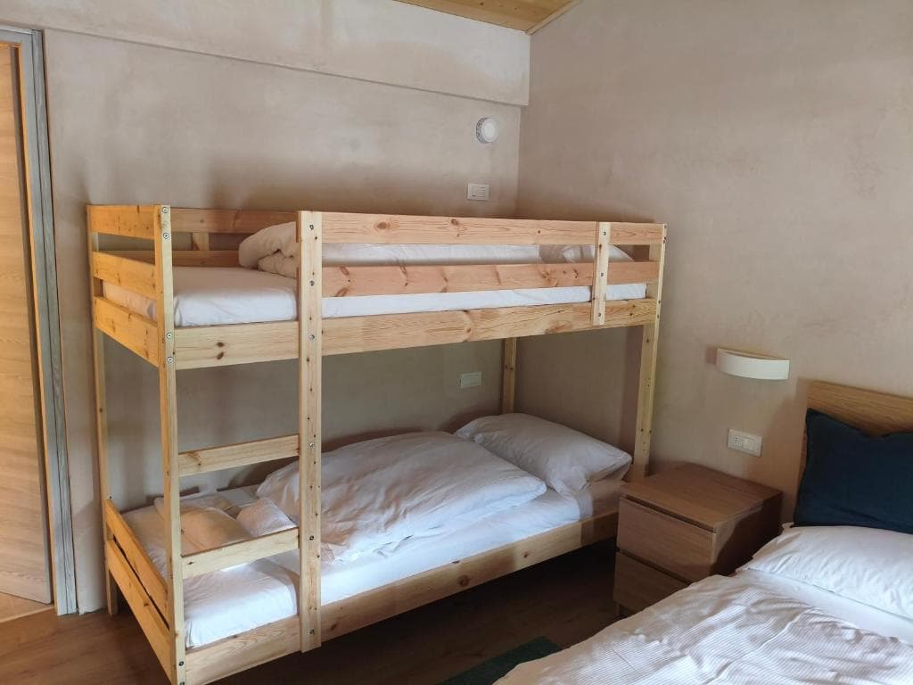 Wooden bunk beds and a single bed with white bedding in a simple room at Rifugio Pelmo.