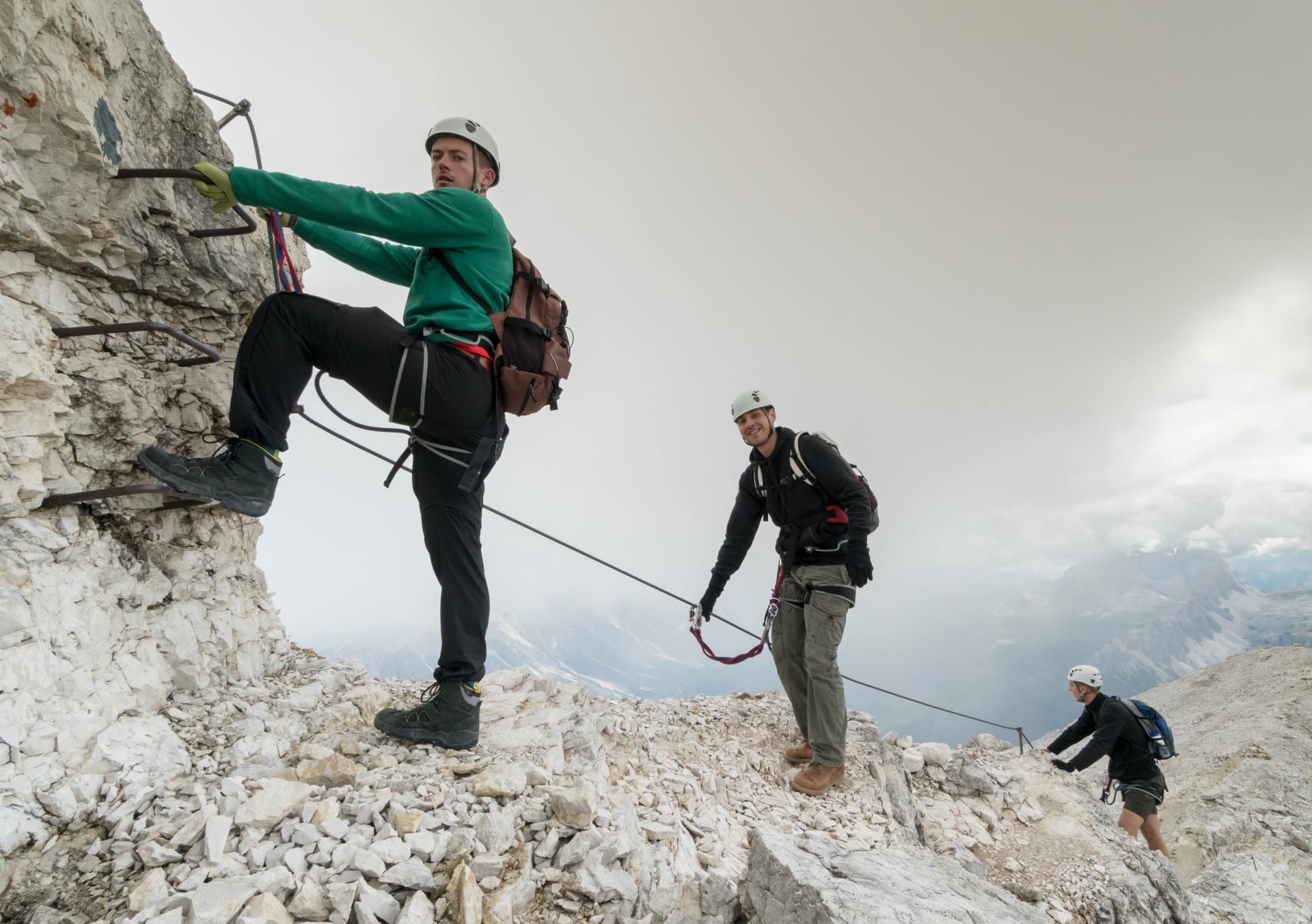 group of young mountain climbers on a steep Via Ferrata with a view of the Italian Dolomites in Alta Badia behind them
