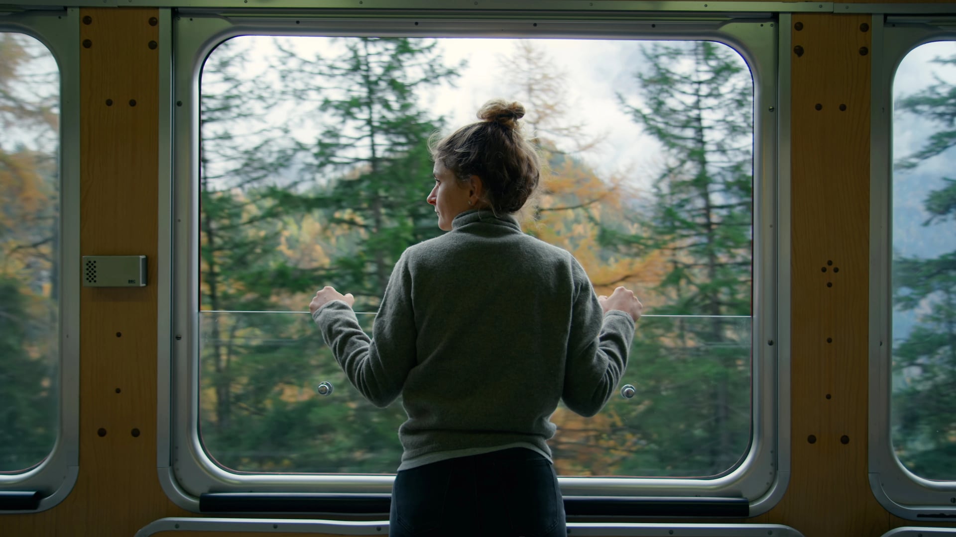 Cinematic and symmetrical beautiful shot of female traveler, travel blogger and inspired adventurer hang out of train window, look at amazing landscape of autumn mountains
