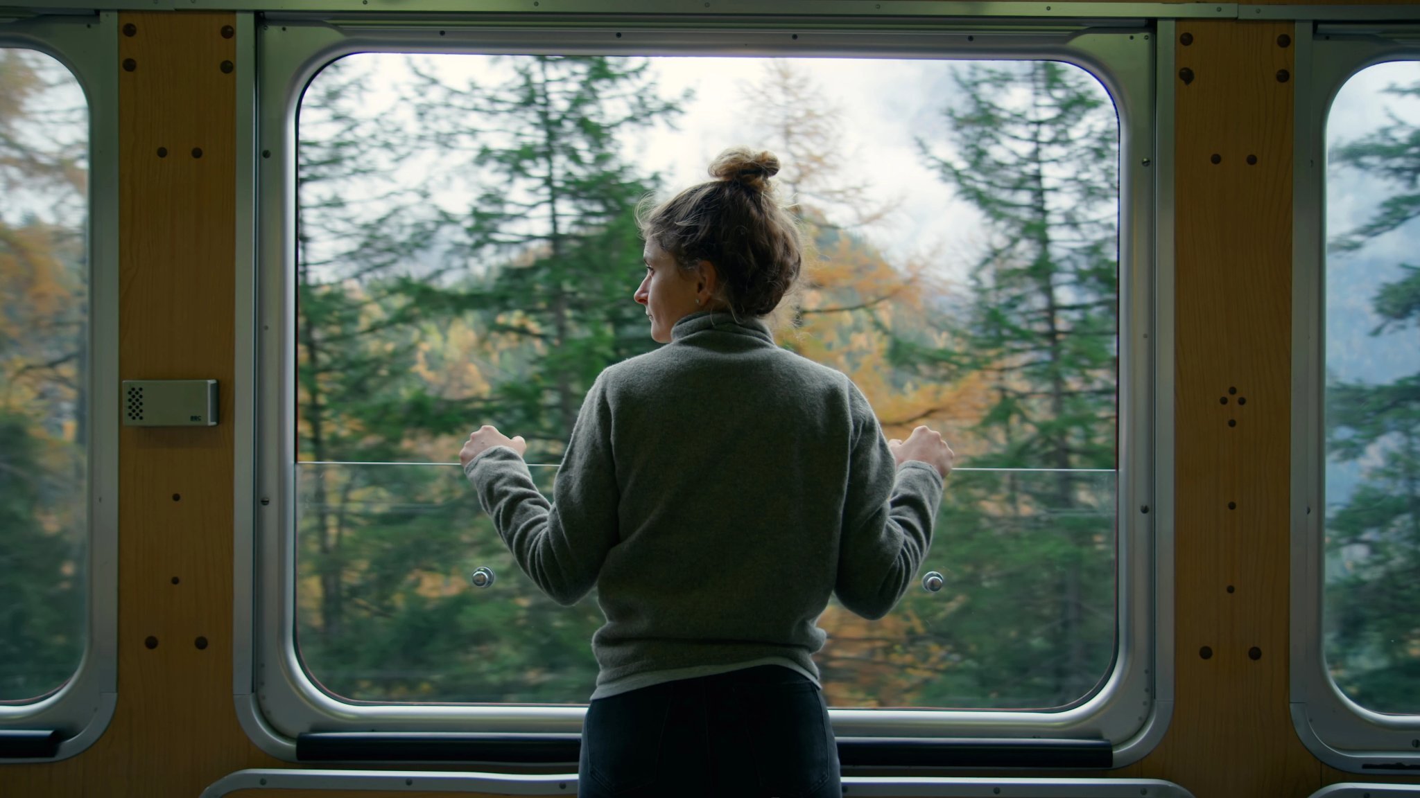 Cinematic and symmetrical beautiful shot of female traveler, travel blogger and inspired adventurer hang out of train window, look at amazing landscape of autumn mountains