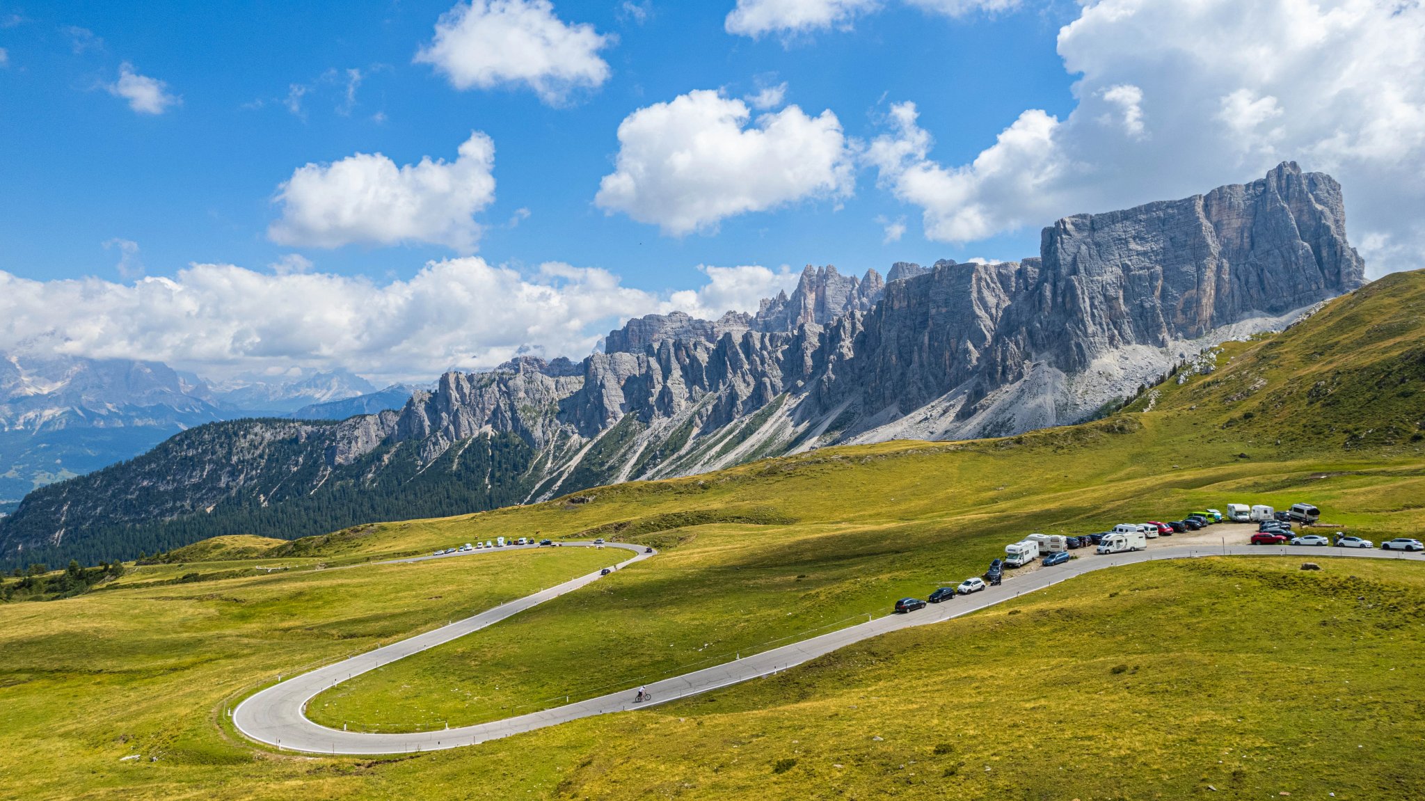 Scenic view of winding road and parked cars beneath the dramatic rocky cliffs of Passo Gardena in the Dolomites Italy