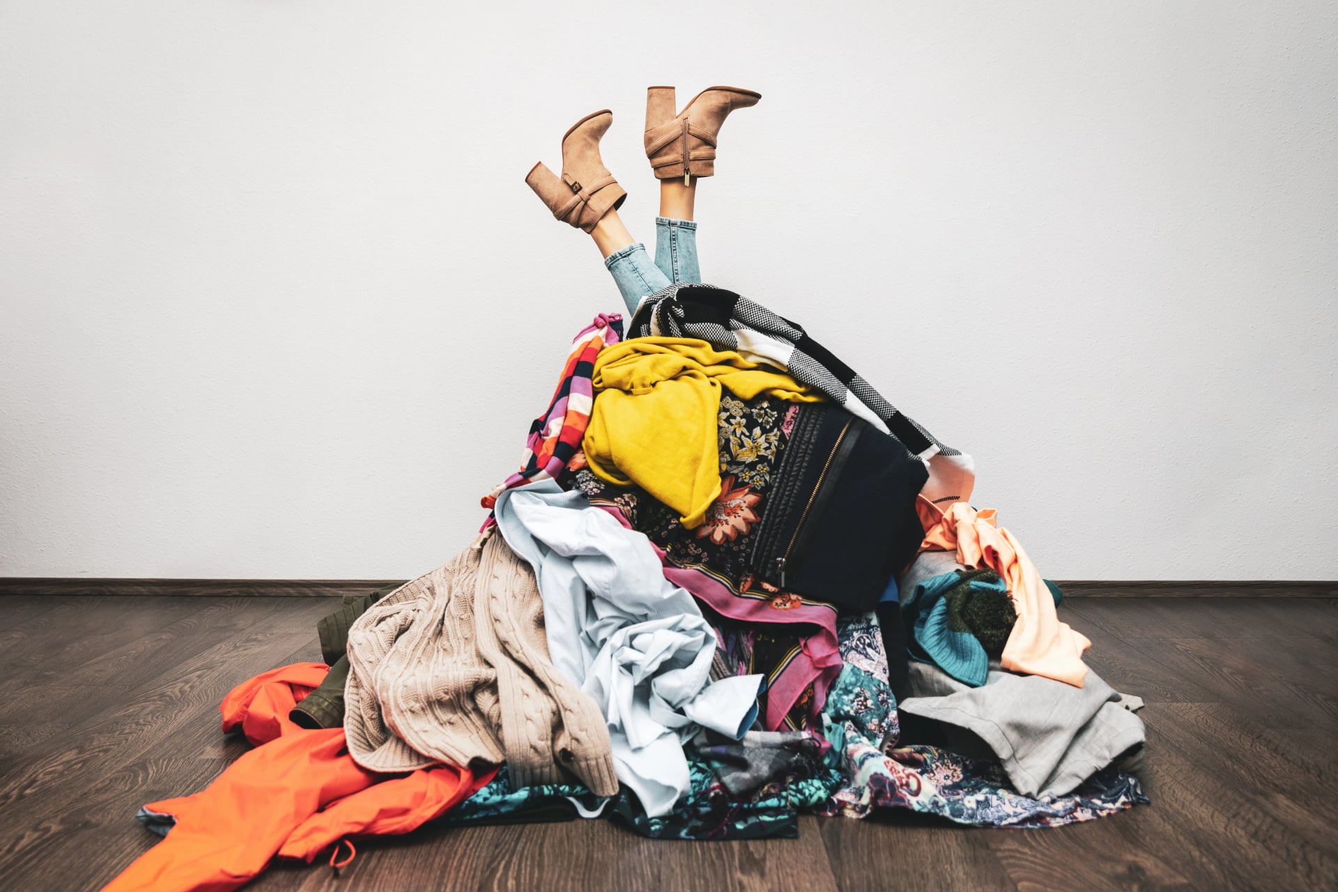 woman legs out of a pile of clothes on the floor. shopping addiction concept