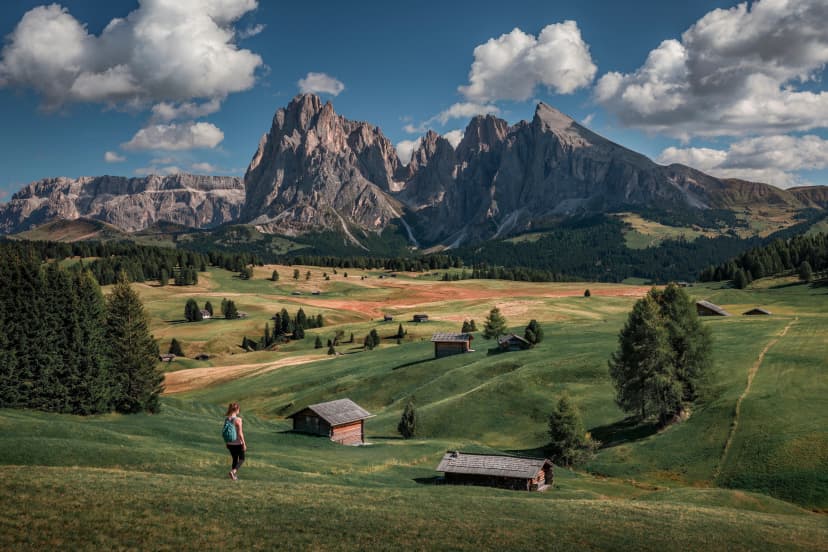 Girl hiking along meadows with wooden cabins at Alpe di Siusi during summer with view to mountains of Plattkofel and Langkofel in the Dolomite Alps in South Tyrol, Italy.