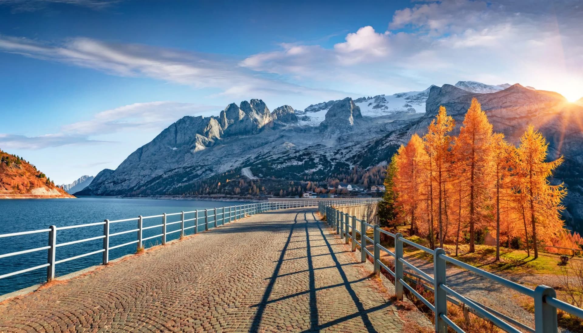 Majestic mountain range on background of walkway on dam on Fedaia lake. Picturesque autumn view of Dolomite Alps. Impressive morning scene of Italy, Europe. Traveling concept background.