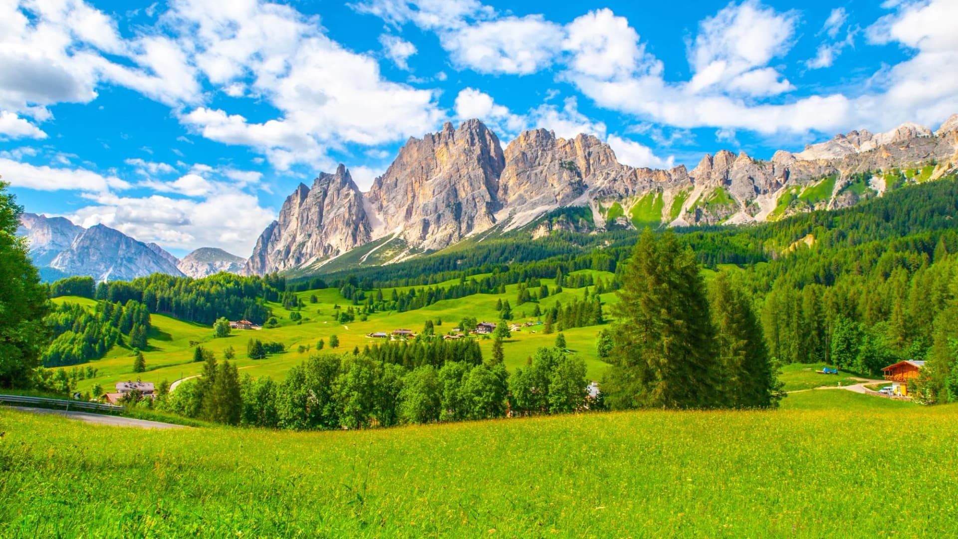 Rocky ridge of Pomagagnon Mountain above Cortina d'Ampezzo with green meadows and blue sky with white summer clouds, Dolomites,, Italy.