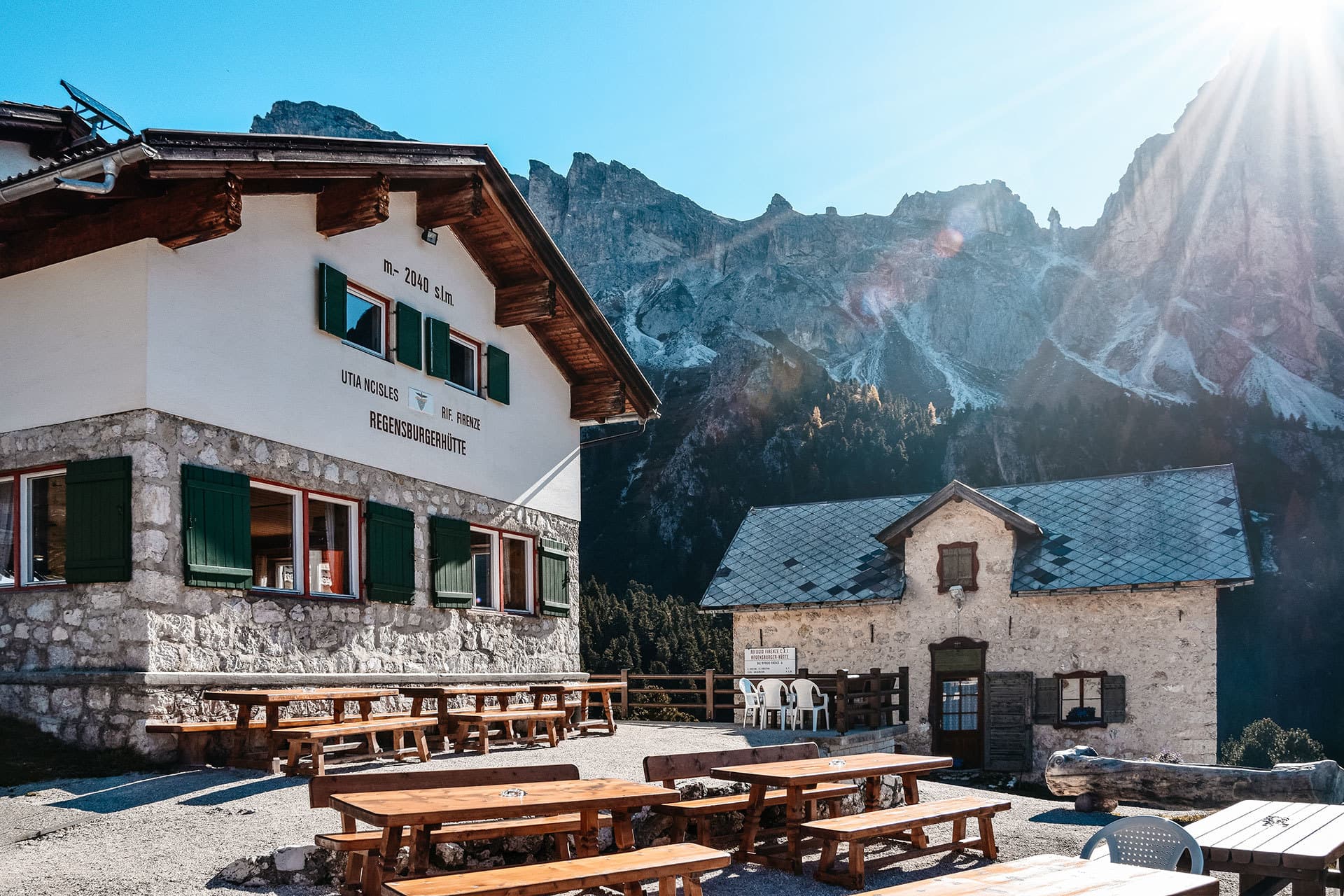 Rifugio Firenze Regensburgerhütte mountain hut with outdoor wooden tables and benches beneath the Dolomite peaks.