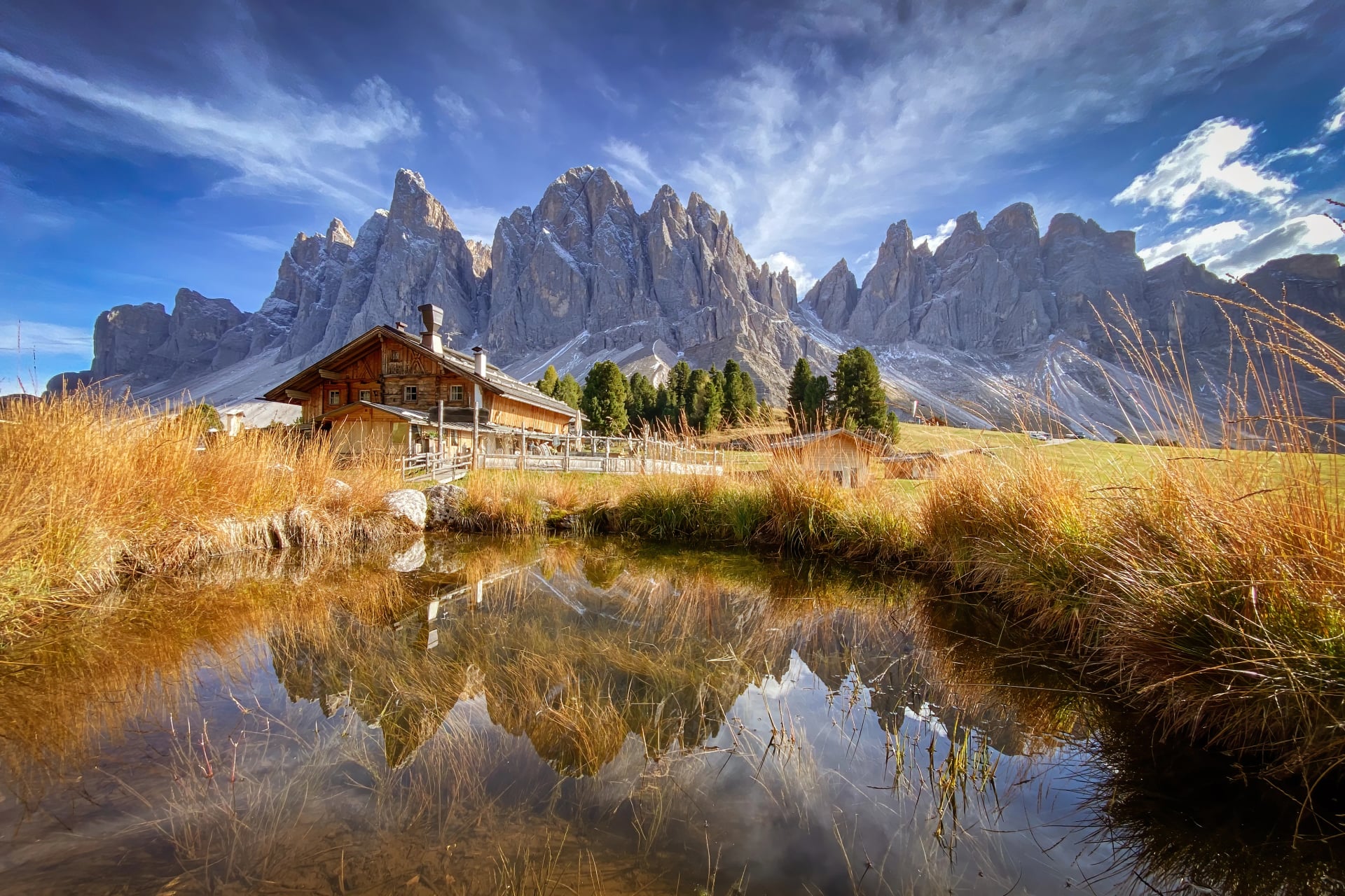 Scenic view of Geisler Alm Rifugio delle Odle in front of dolomites mountains and reflection in the water of a pond, South Tyrol, Italy