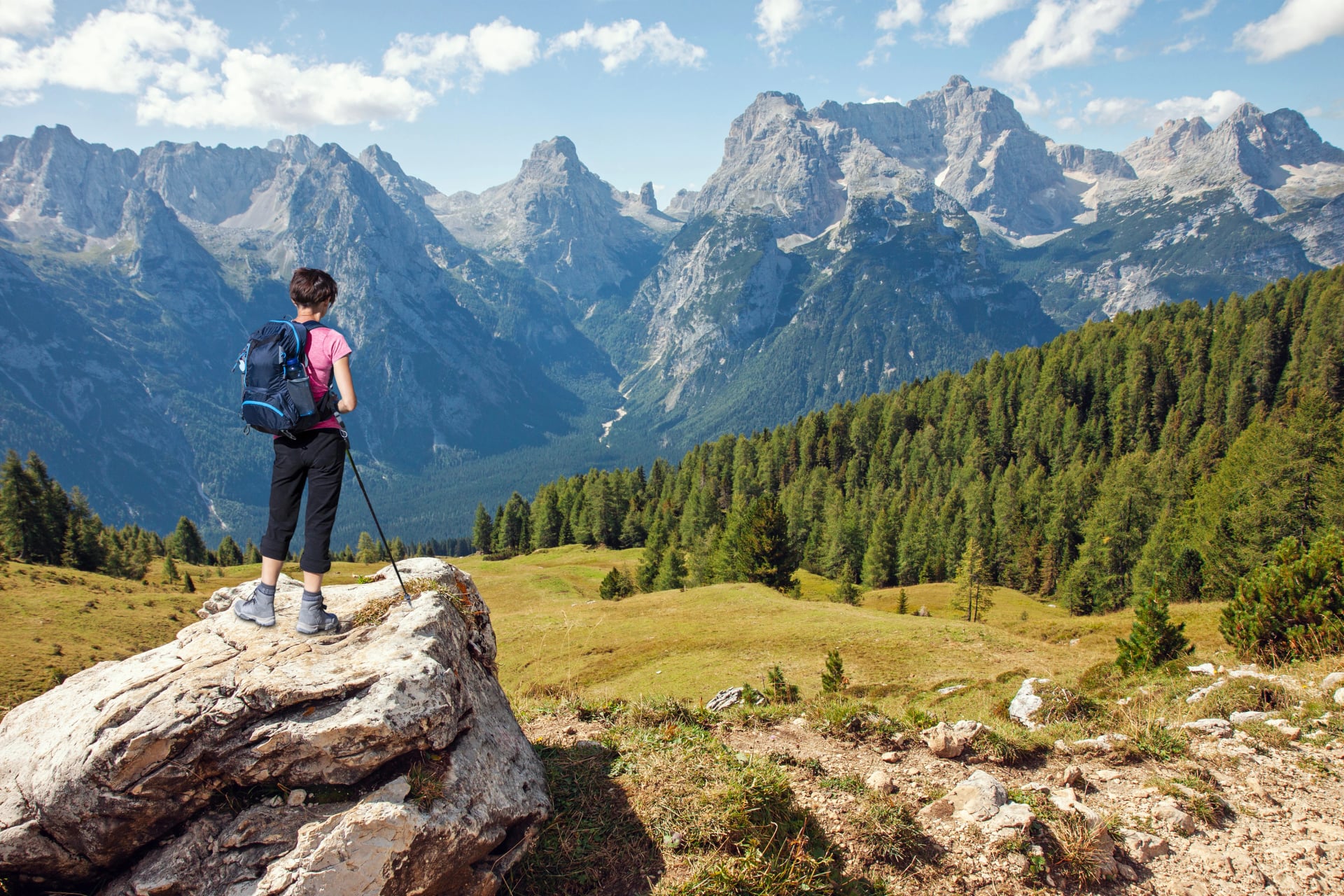 Woman hiker standing on stone rock and looking at scenic mountains in summer