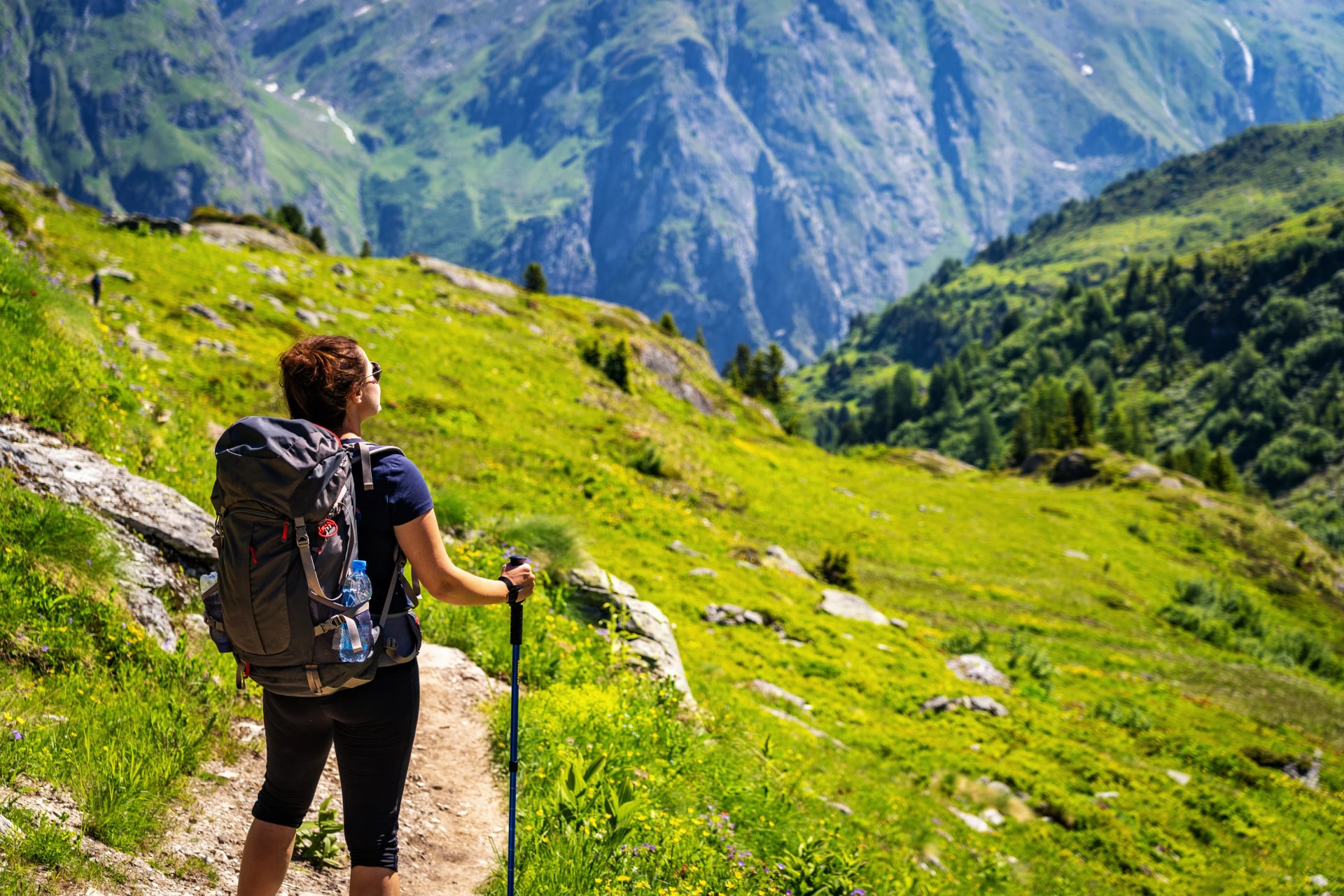 Female traveler with backpack hiking mountain trail and admiring views of Swiss Alps in Val de Bagnes area, Switzerland.