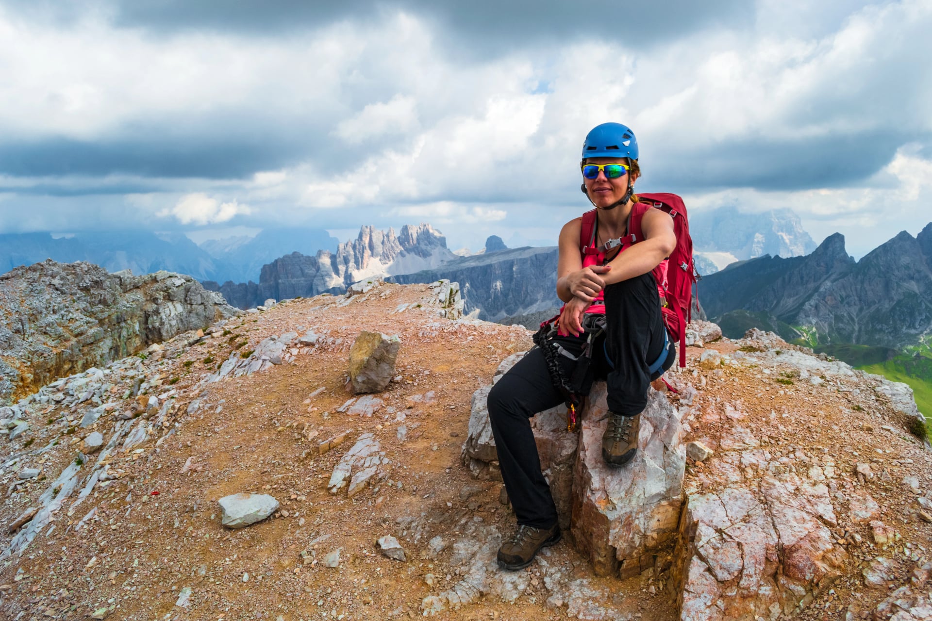 Female climber on Averau peak at the end of a via ferrata route, with dark storm clouds approaching in the background, in the Dolomite mountains, Italy. Tourism in Europe in the summer.