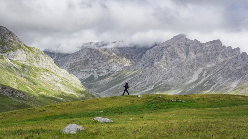 Hiker climbing a rocky, grassy slope in a mountainous landscape, with misty clouds above. Dressed in outdoor gear, perfect for themes of adventure, nature, hiking, and exploration in the wilderness