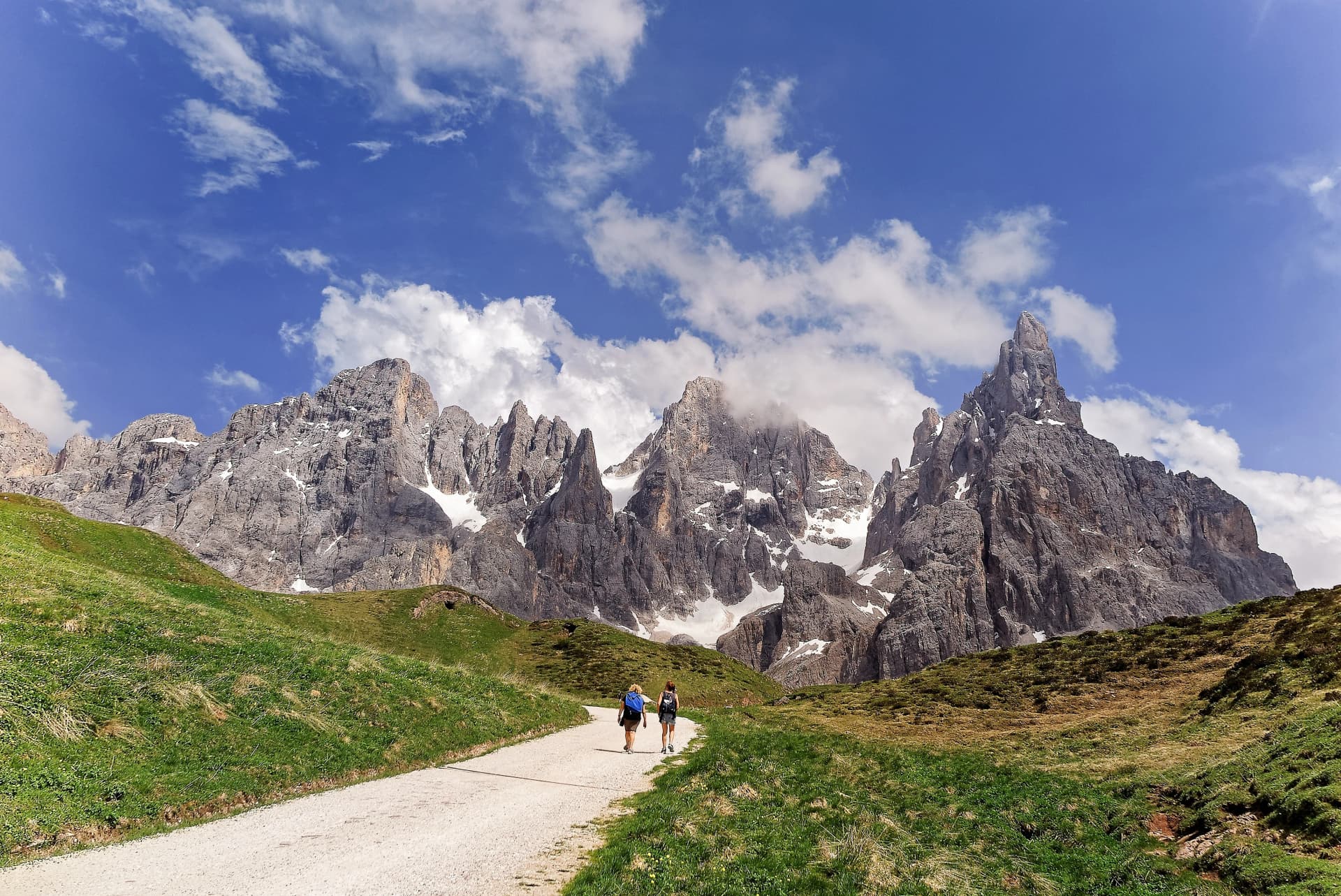 Tourists hiking on a track towards Cimon della Pala amid rugged peaks of Pale di San Martino mountain range in Dolomites on a sunny summer day, in Passo Rolle, Trentino Alto Adige, South Tyrol, Italy