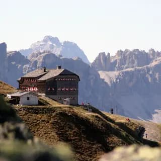 Sillianer Hütte mountain hut on a grassy ridge with rocky Dolomite peaks in the background.
