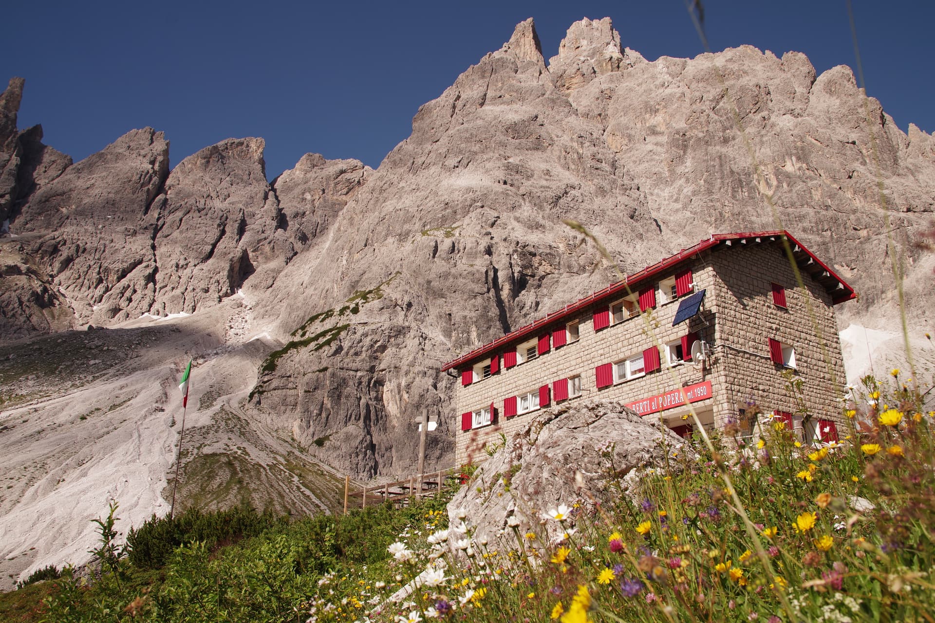 Rifugio Berti mountain hut with red shutters and wildflowers in the Italian Dolomites.