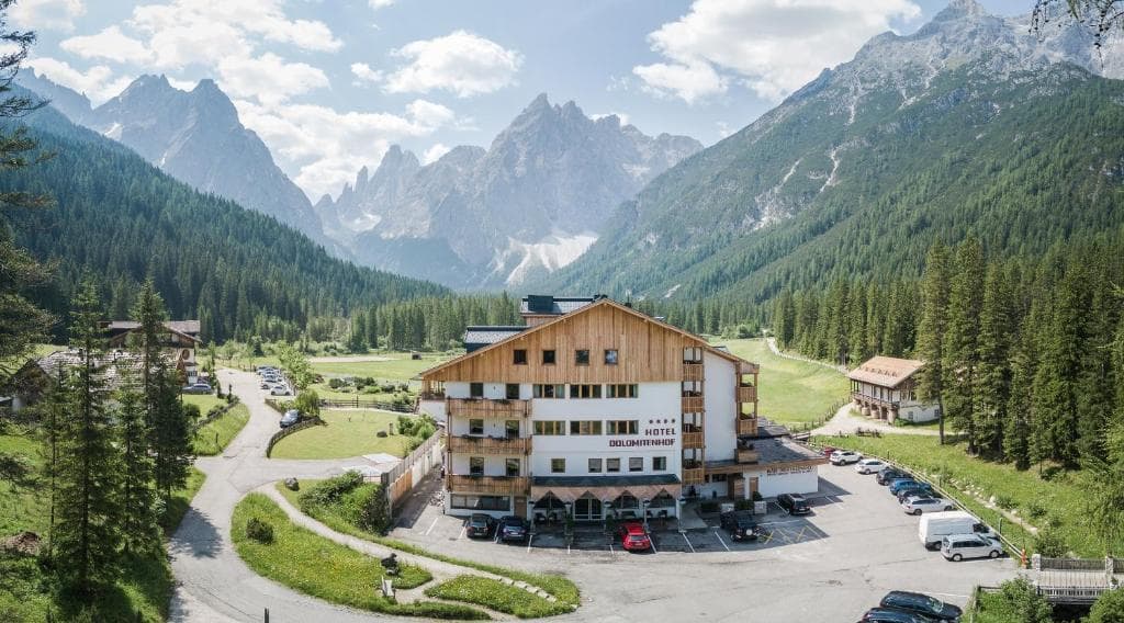 Hotel Dolomitenhof in the Italian Dolomites with surrounding mountain peaks and pine forest.