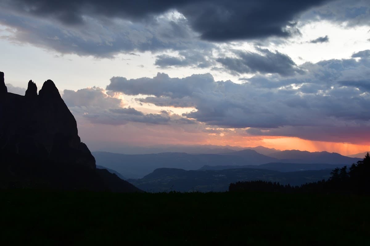 Mountain peaks silhouetted against a cloudy sunset sky with distant ranges
