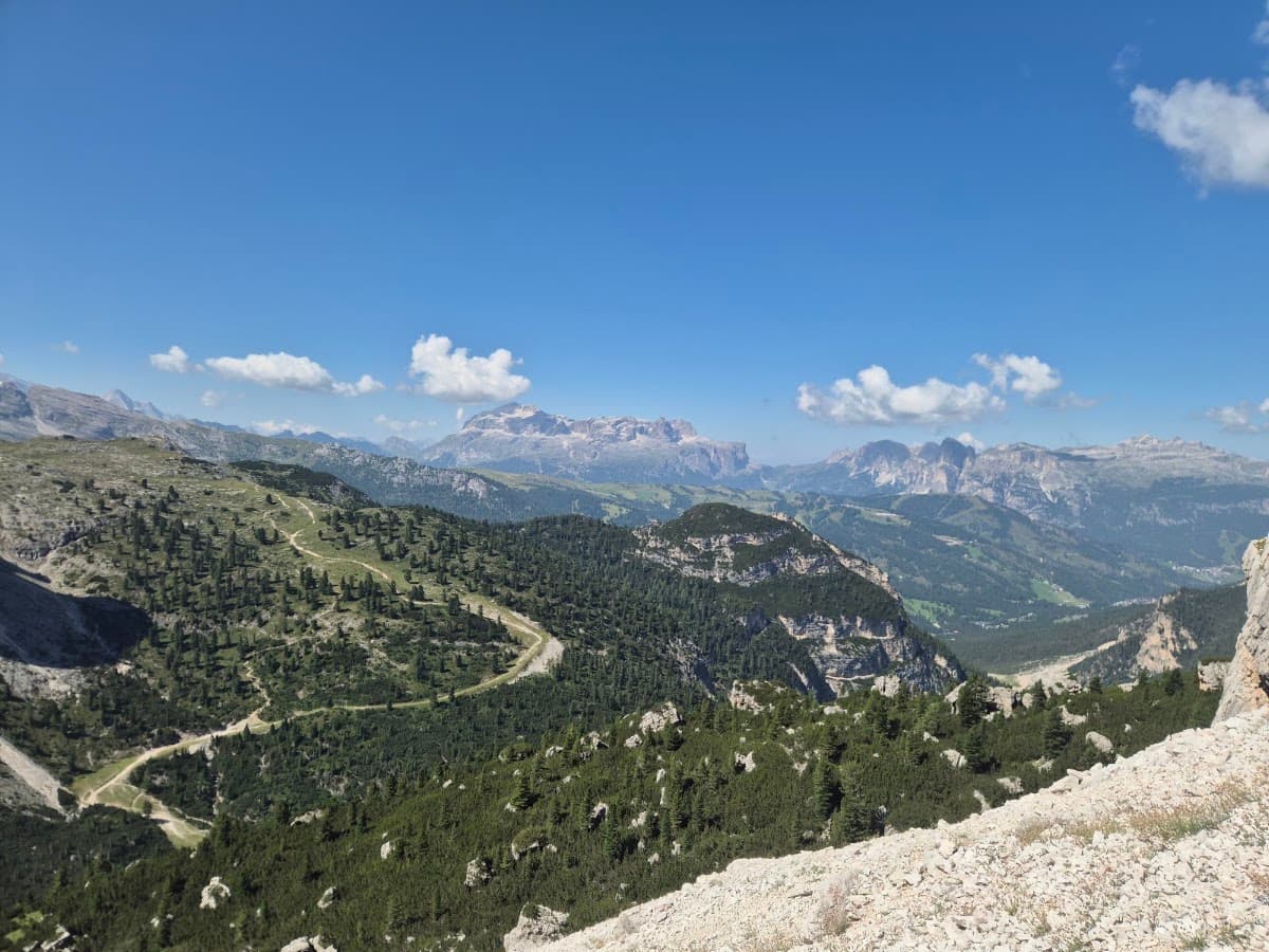 Alpine mountain landscape with winding trail, forests, and blue sky