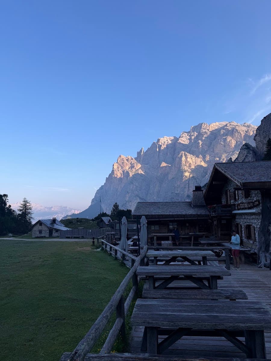 Wooden picnic tables on outdoor terrace of alpine mountain hut with rocky peaks in background